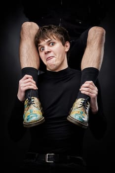 young handsome guy hugs male legs in bright shoes on black background. fashion