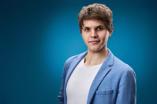 young guy in jacket looking at the camera on blue studio background. copy space