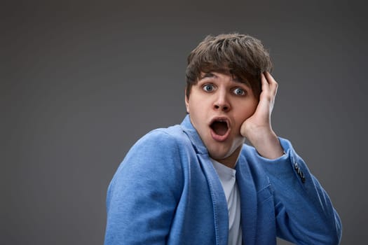 shocked man with surprise expression, fear and excited face on gray studio background. close-up