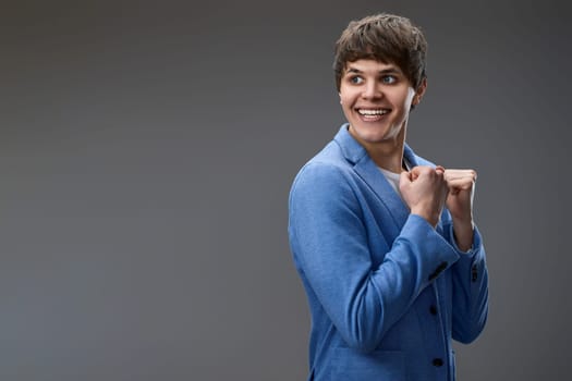 very excited young man showing victory gesture holding fists raising hands up on gray background. copy space