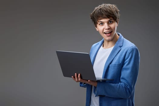 Portrait of caucasian young student man holding laptop isolated on gray background. websurfing