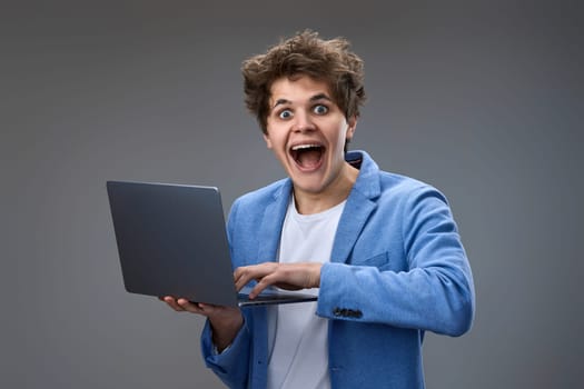 Funny and crazy caucasian nerd man with laptop on gray background