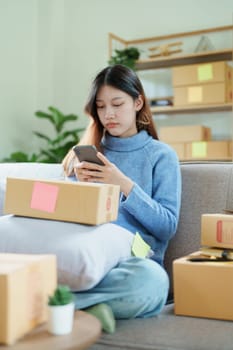 Starting small business entrepreneur of independent Asian woman smiling using computer laptop with cheerful success of online marketing package box items and SME delivery concept.