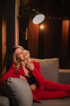 a beautiful girl dressed in a red formal suit posing in a modern interior.