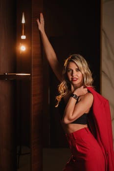 a beautiful girl dressed in a red formal suit posing in a modern interior.