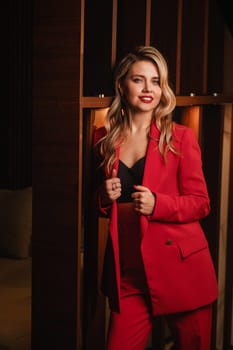 a beautiful girl dressed in a red formal suit posing in a modern interior.