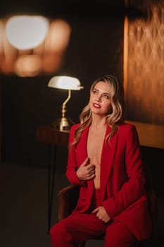 a beautiful girl dressed in a red formal suit posing in a modern interior.