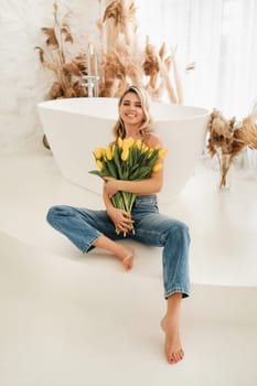 Cute smiling girl with a bouquet of yellow tulips in the interior.