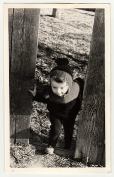 HODONIN, THE CZECHOSLOVAK REPUBLIC - CIRCA 1942: A vintage photo shows small girl goes through the hole in wooden fence.