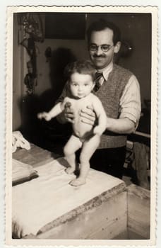 HODONIN, THE CZECHOSLOVAK REPUBLIC - CIRCA 1940: A vintage photo shows small baby girl after having a bath. Wooden wasthub is near.