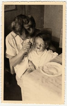 HODONIN, THE CZECHOSLOVAK REPUBLIC - CIRCA 1942: A vintage photo shows small toddler girl and mother feeds her.