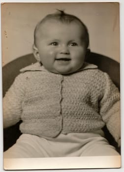 THE CZECHOSLOVAK SOCIALIST REPUBLIC - CIRCA 1960s: Vintage portrait shows toddler girl sits on armchair. Black & white antique photo.