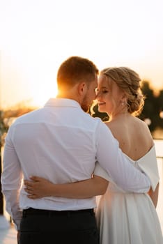 bride and groom against the backdrop of a yellow sunset on a pier near the river