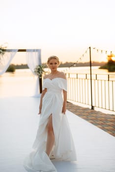 bride against the background of a yellow sunset on a pier near the river