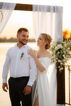 bride and groom against the backdrop of a yellow sunset on a pier near the river