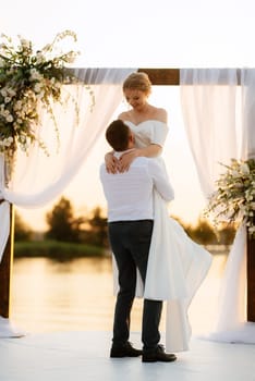 bride and groom against the backdrop of a yellow sunset on a pier near the river