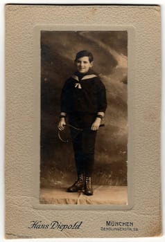 MUNICH, GERMANY - CIRCA 1910: Vintage cabin card shows young boy wears sailor costume and holds tennis racket.
