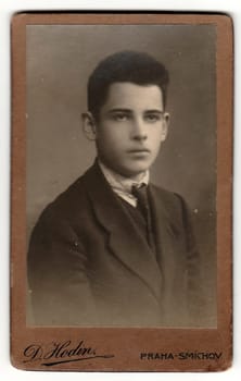 PRAGUE, THE CZECHOSLOVAK REPUBLIC - CIRCA 1920s: Vintage cabinet card shows young boy wears posh garment. Antique black white photo with sepia tint.