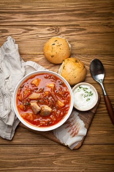 Ukrainian Borscht, red beetroot soup with meat, in white bowl with sour cream, garlic buns Pampushka and salo slices on rustic stone background. Traditional authentic dish of Ukraine