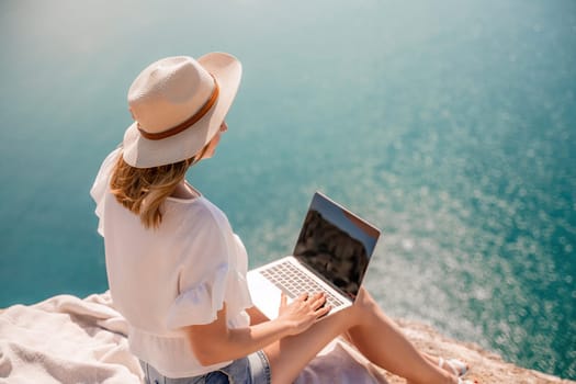 Freelance women sea working on the computer. Good looking middle aged woman typing on a laptop keyboard outdoors with a beautiful sea view. The concept of remote work