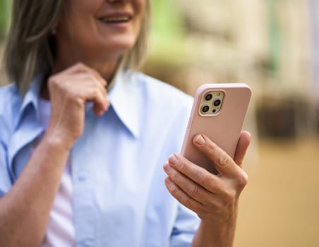 Close-up photo captures hands of elderly woman holding smartphone in old city. The senior woman's smile and positive expression convey sense of happiness and connection through technology. High quality photo
