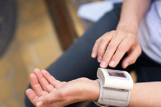 Close-up of elderly woman's hands holding pressure measurement device outdoors. The image portrays the concept of health monitoring, diagnosis, and healthcare for seniors. High quality photo