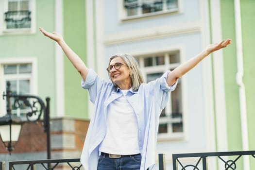 Mature woman standing in old city, smiling and raising her hands to sky, expressing happiness and positive emotions. Perfect illustration of happiness in everyday life and senior living. High quality photo