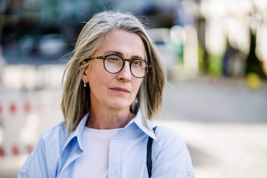 Sad mature woman with silver hair and glasses in a European city, portraying feelings of loneliness, depression, and despair in the context of aging and mental health issues in seniors. High quality photo