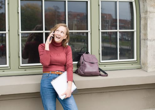 a young caucasian girl returns to college, stands with a backpack and notebooks and talks on the phone in a laugh, back to school, High quality photo