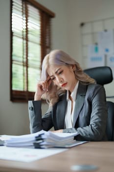 Portrait of a young Asian woman showing a serious face as she using financial documents and computer laptop on her desk in the early morning hours.