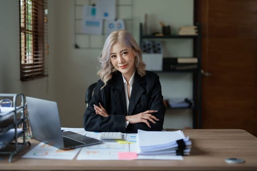 Portrait of a woman business owner showing a happy smiling face as he has successfully invested her business using computers and financial budget documents at work.