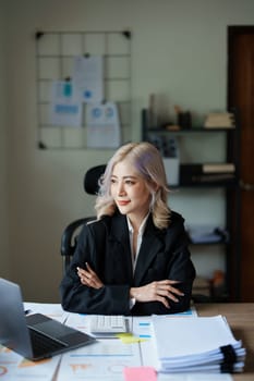 Portrait of a thoughtful Asian businesswoman looking at financial statements and making marketing plans using a computer on her desk.