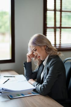 Portrait of a young Asian woman showing a serious face as she using financial documents and computer laptop on her desk in the early morning hours.