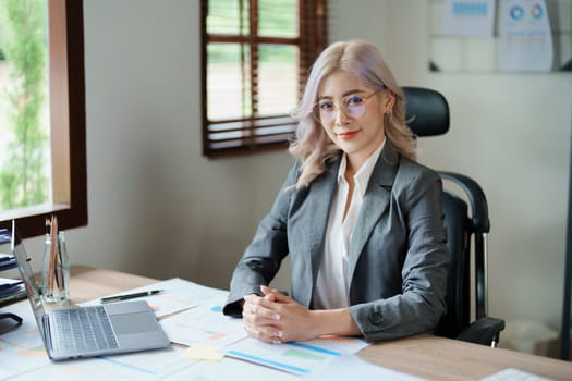 Portrait of a woman business owner showing a happy smiling face as he has successfully invested her business using computers and financial budget documents at work.