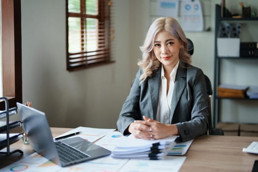 Portrait of a woman business owner showing a happy smiling face as he has successfully invested her business using computers and financial budget documents at work.