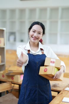 Starting small business entrepreneur of independent Asian woman smiling using computer laptop with cheerful success of online marketing package box items and SME delivery concept.