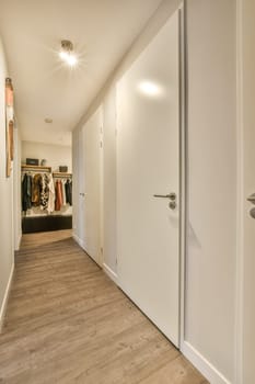 a hallway with white walls and wood flooring the room is well lit by recessed light fixtures on the ceiling