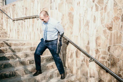 Portrait of a senior professional man in a suit with various problems. A middle-aged businessman with a briefcase descends the stairs.