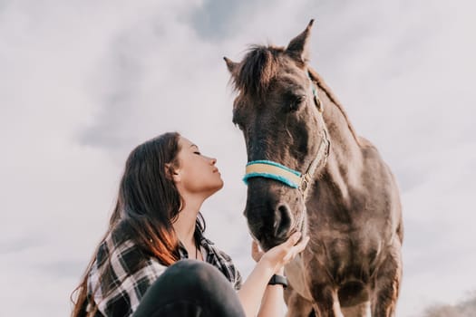 Cute happy young woman with horse. Rider female drives her horse in nature on evening sunset light background. Concept of outdoor riding, sports and recreation.