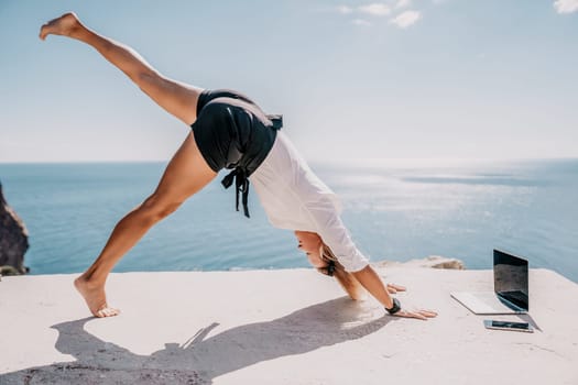 Happy girl doing yoga with laptop working at the beach. beautiful and calm business woman sitting with a laptop in a summer cafe in the lotus position meditating and relaxing. freelance girl remote work beach paradise