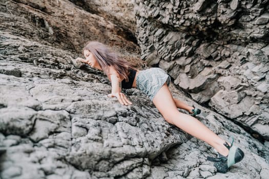 A girl climbs a rock. The athlete trains in nature. Woman overcomes difficult climbing route. Extreme hobby. Tourist woman rock climber hiking on mountains rocks over beautiful sea coast