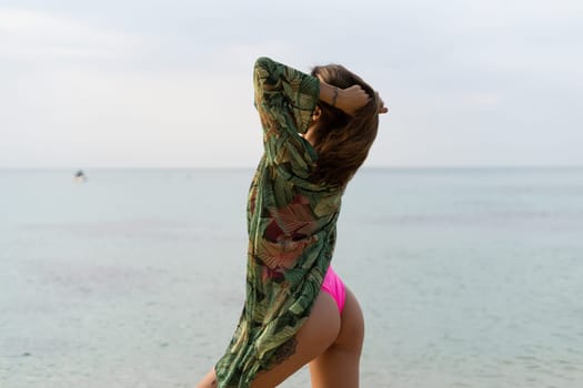 Stylish romantic tender athletic slim sensual woman in pink swimsuit, tropical kimono and sunglasses on the beach at sunset