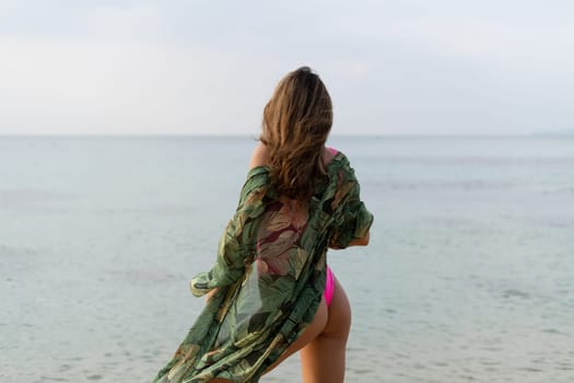 Stylish romantic tender athletic slim sensual woman in pink swimsuit, tropical kimono and sunglasses on the beach at sunset