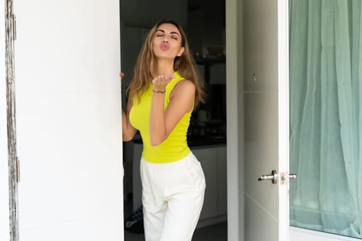 Welcome. Portrait of cheerful woman standing in doorway of modern apartment, greeting visitor and inviting guest to enter her home, happy