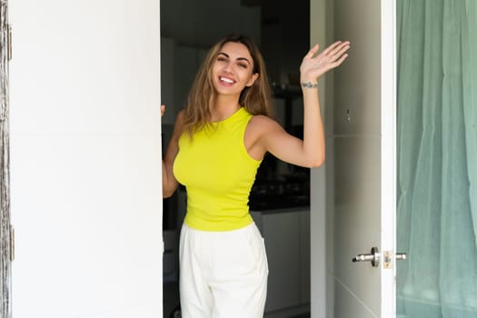 Welcome. Portrait of cheerful woman standing in doorway of modern apartment, greeting visitor and inviting guest to enter her home, happy