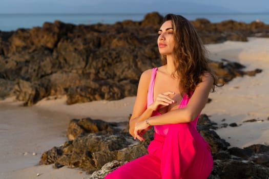 Fashion stylish beautiful sensual young woman, slim, in fashionable bright pink pants and bodysuit on a tropical beach at sunset posing