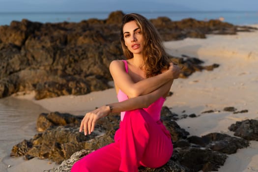 Fashion stylish beautiful sensual young woman, slim, in fashionable bright pink pants and bodysuit on a tropical beach at sunset posing