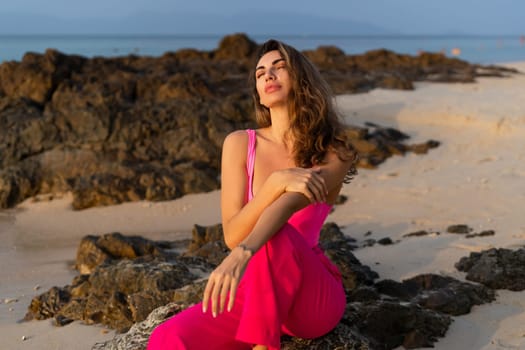 Fashion stylish beautiful sensual young woman, slim, in fashionable bright pink pants and bodysuit on a tropical beach at sunset posing