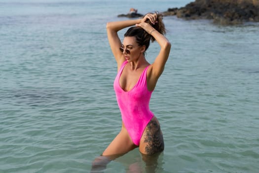 Stylish romantic tender, athletic body good shape, slim sensual woman in a pink swimsuit and sunglasses on the beach at sunset