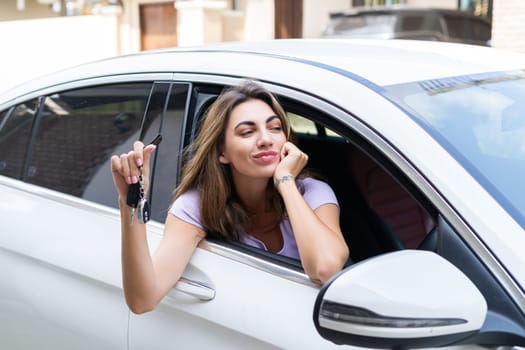 Beautiful young happy smiling woman driving her car, showing the keys to a new car